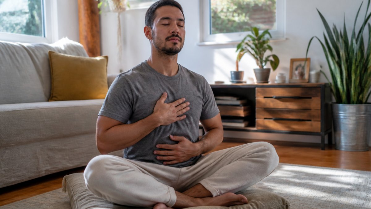 Person practicing deep breathing exercises for anxiety while sitting on a cushion in a sunlit living room.